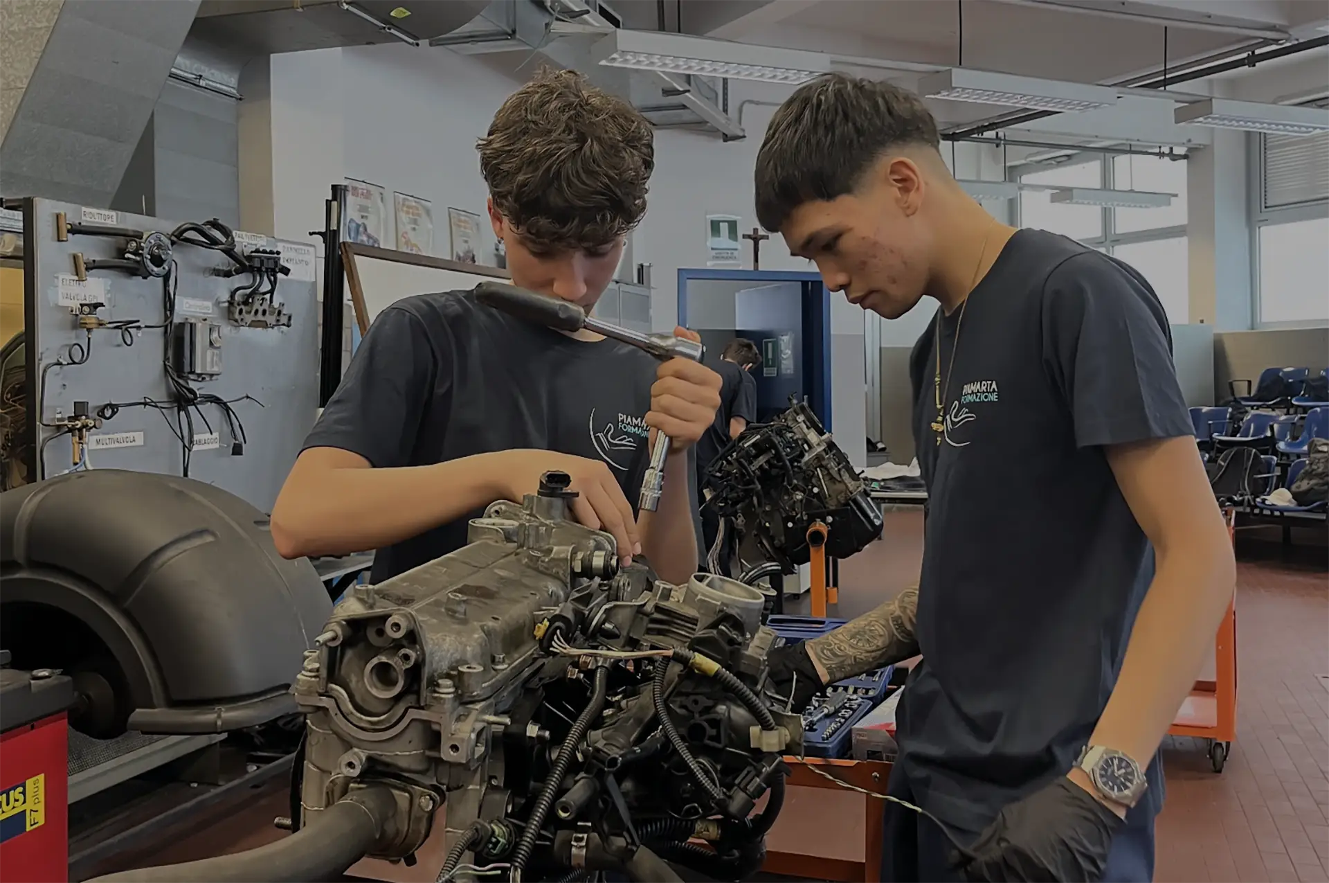 Due studenti in una lezione pratica di meccanica mentre lavorano su un motore, utilizzando attrezzi professionali in un'officina scolastica.