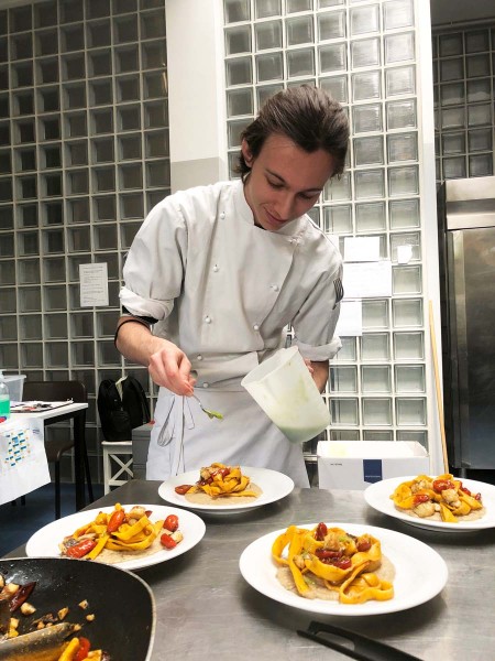 Chef che impiatta un piatto di pasta con pomodorini in una cucina professionale