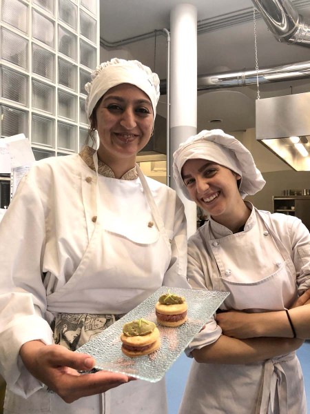 Due chef sorridenti in cucina mostrano un vassoio di dolci gourmet