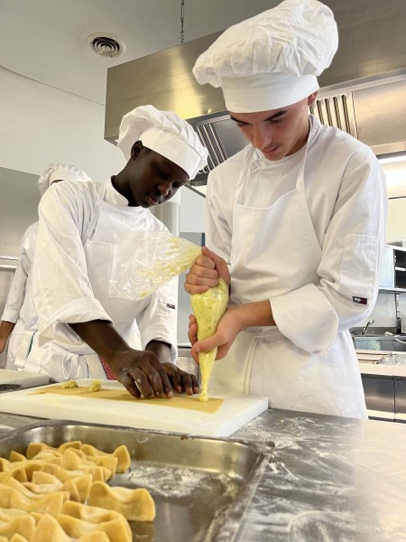 Due chef mentre preparano ravioli in cucina, utilizzando una sacca da pasticciere per il ripieno