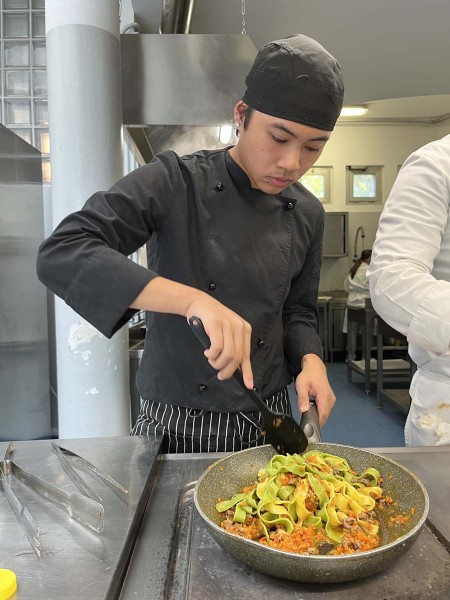 Chef in cucina mentre mescola una padella di tagliatelle con ragù