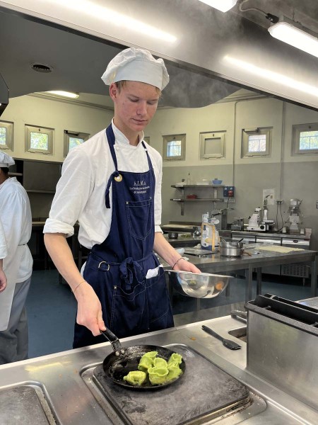 Chef in cucina mentre salta dei ravioli verdi in padella