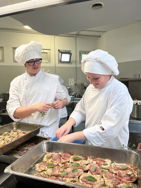 Due chef in cucina preparano teglie di carne con salvia e prosciutto