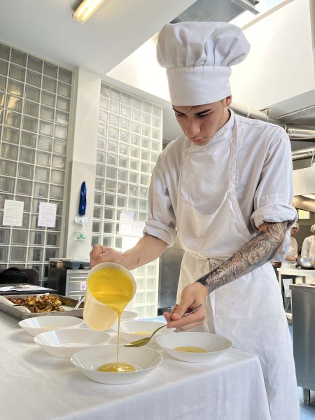 Chef in cucina mentre versa una crema gialla in piatti fondi