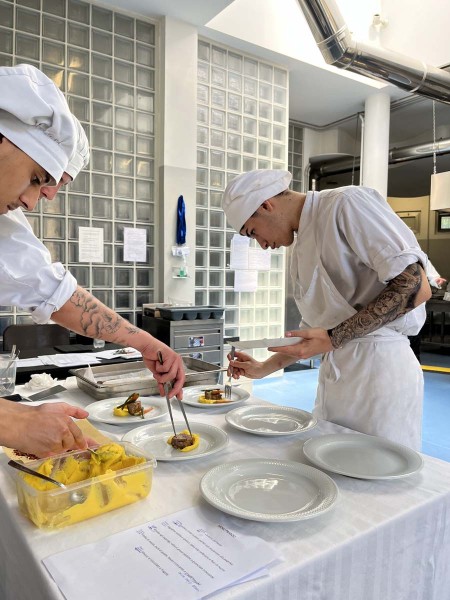 Due chef impiattano carne con crema gialla e verdure in cucina