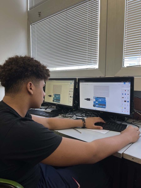 Studente che utilizza un computer per lavorare su un progetto Arduino, con due monitor che mostrano il layout di un circuito.