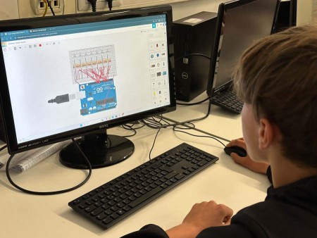 Studente lavora su un progetto di Arduino visualizzato su un monitor in un'aula informatica.