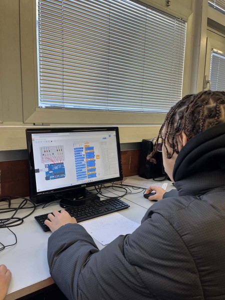 Studente al computer lavora su un progetto di programmazione utilizzando Arduino in un'aula informatica.