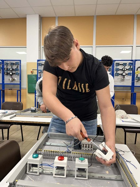 Studente che lavora su un pannello elettrico, utilizzando un cacciavite per collegare componenti elettronici in un'aula laboratorio.