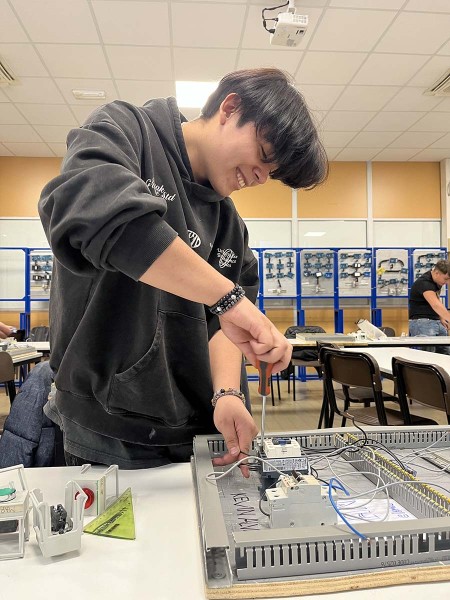 Studente sorridente impegnato nel montaggio di un quadro elettrico durante una lezione pratica in laboratorio.