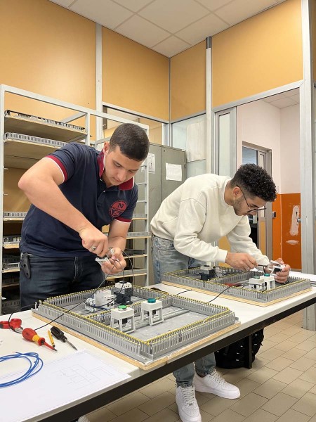 Due studenti intenti a cablare e montare quadri elettrici durante un'esercitazione pratica in laboratorio.