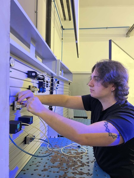Studente mentre collega componenti su un pannello di controllo pneumatico in laboratorio, durante un'esercitazione pratica di meccanica ed elettrotecnica.
