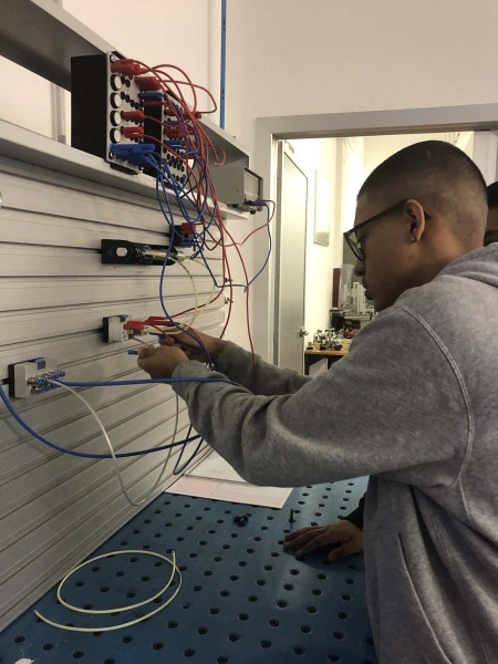 Uno studente in un laboratorio tecnico collega cavi a un pannello elettrico durante un'attività pratica di cablaggio.