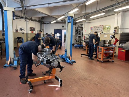 Meccanici al lavoro su motori in un'officina con attrezzature professionali e sollevatori per auto.