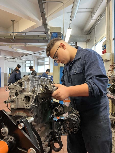 Giovane meccanico che lavora su un motore in officina, concentrato sull'assemblaggio di un componente.