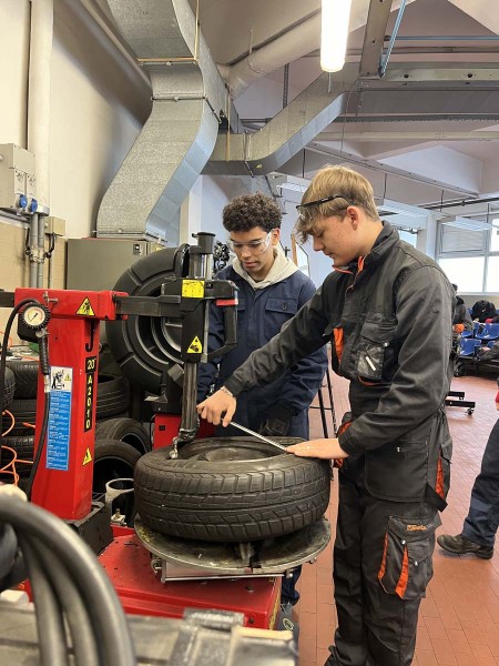 Due giovani meccanici utilizzano una macchina per il montaggio di pneumatici in officina.