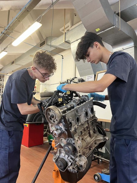 Due giovani meccanici lavorano insieme su un motore in officina, concentrati sui dettagli tecnici.