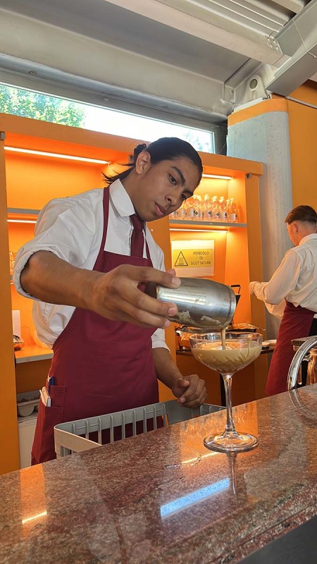 Giovane barista versa un cocktail in un bicchiere da martini dietro il bancone di un bar.