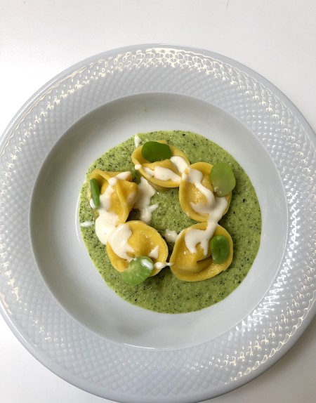 Piatto di tortelli su crema verde con salsa bianca e fave, presentato su un piatto bianco.