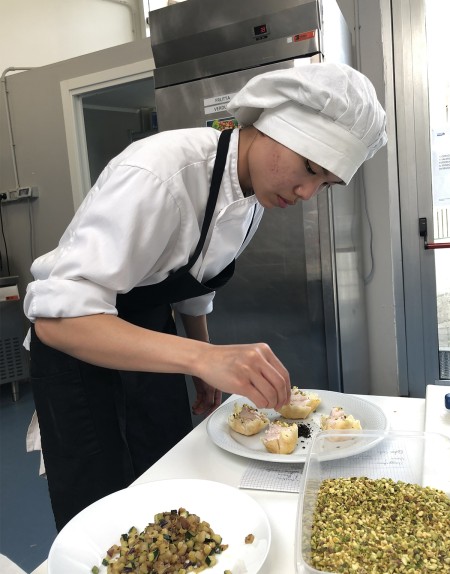 Giovane chef decora un piatto in una cucina professionale, concentrato sui dettagli.