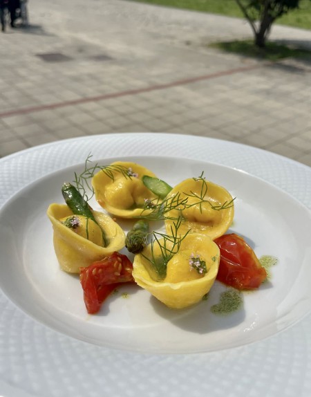 Tortelli guarniti con asparagi e pomodorini, decorati con erbe aromatiche, serviti su un piatto bianco.
