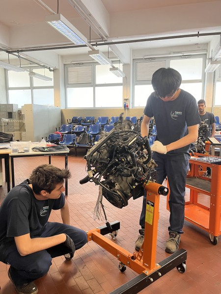 Due giovani meccanici lavorano insieme su un motore montato su un supporto in officina.