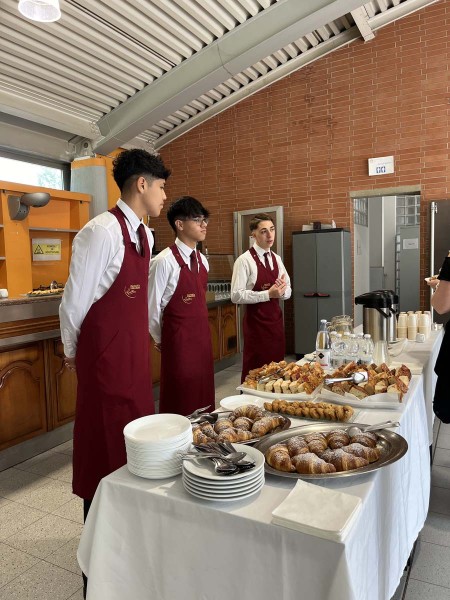 Tre camerieri in grembiule rosso in piedi vicino a un tavolo apparecchiato con cibo e bevande per un buffet