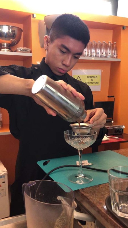 Bartender che versa un drink da uno shaker in un bicchiere da cocktail al bancone