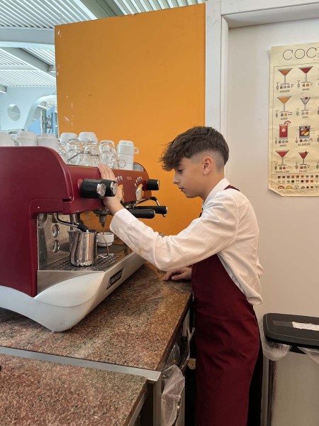 Cameriere in grembiule rosso prepara il caffè con una macchina da espresso