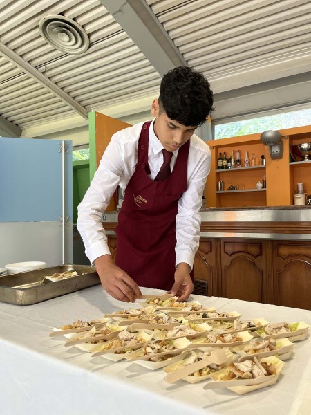 Cameriere in grembiule rosso prepara piatti di antipasti su un tavolo apparecchiato