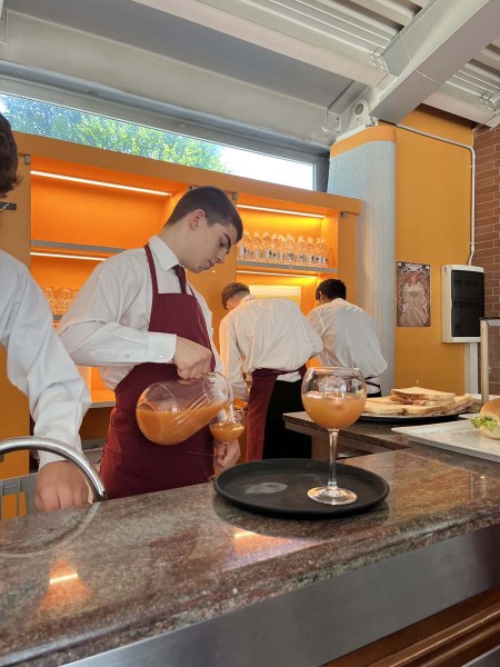 Cameriere in grembiule rosso versa una bevanda da una caraffa in un bicchiere al bancone