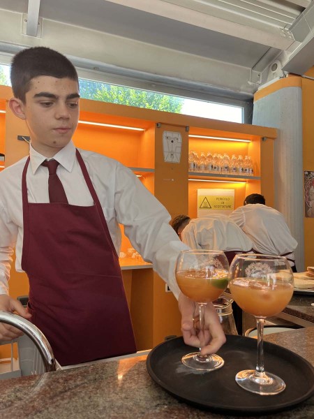 Cameriere in grembiule rosso serve due bicchieri di cocktail su un vassoio